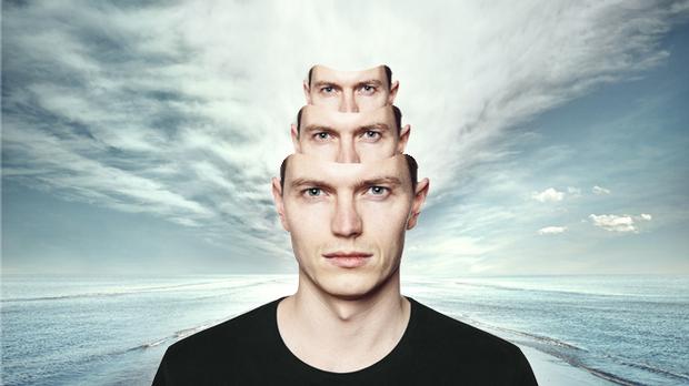 man with two copies of his face nesting on top of his head, with ocean and sky behind him